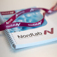 NordLab-muistiinpanolehtiö, jonka päällä on NordLabin avainnauha.