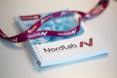 NordLab-muistiinpanolehtiö, jonka päällä on NordLabin avainnauha.